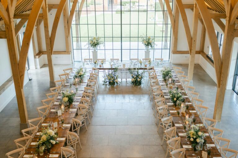 Long feasting tables in a U shape on the limestone floor, seen from above, with the lawn through the glass gable, The Post Barn