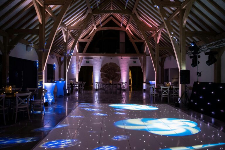 The barn set up for the evening with a starlit dance floor and coloured uplighting, The Post Barn