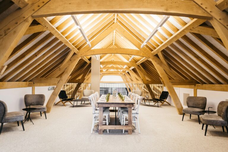 The Rafters mezzanine under the oak roof, set with a long table and lounge chairs, The Post Barn
