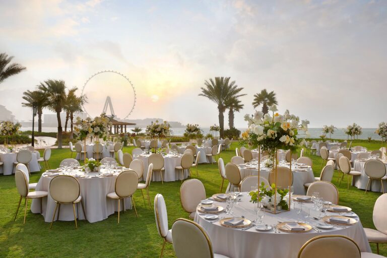 Round tables set for a wedding dinner on La Brise Lawn at sunset, The Ritz-Carlton, Dubai