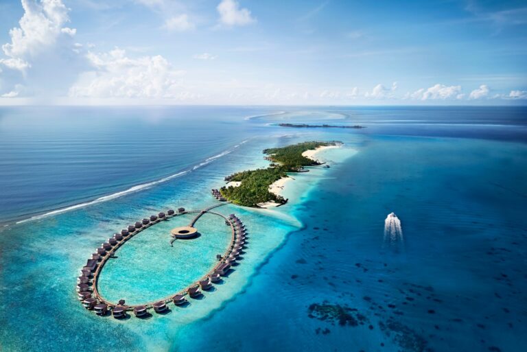 The resort and its overwater villa ring from above, with a boat in the lagoon, The Ritz-Carlton Maldives, Fari Islands
