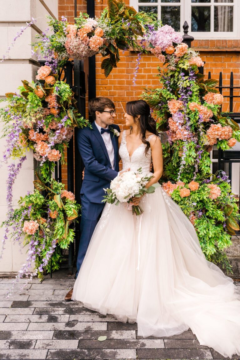 A couple beneath a floral arch of peach roses and wisteria outside the hotel entrance, The Roseate Reading