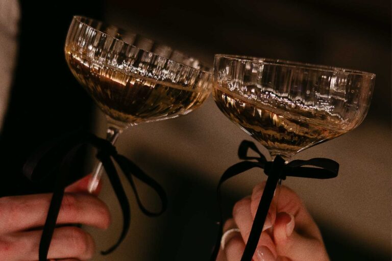 Two vintage coupes of champagne tied with black ribbon, raised for a toast, The Roseate Reading