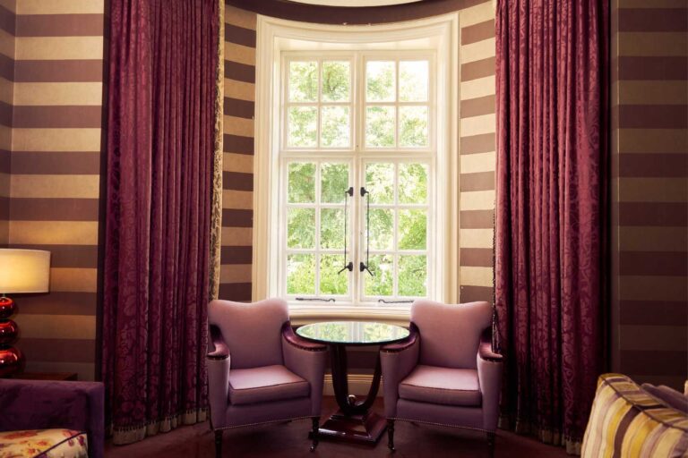 A bay window with two armchairs and heavy curtains, looking out to trees, The Roseate Reading