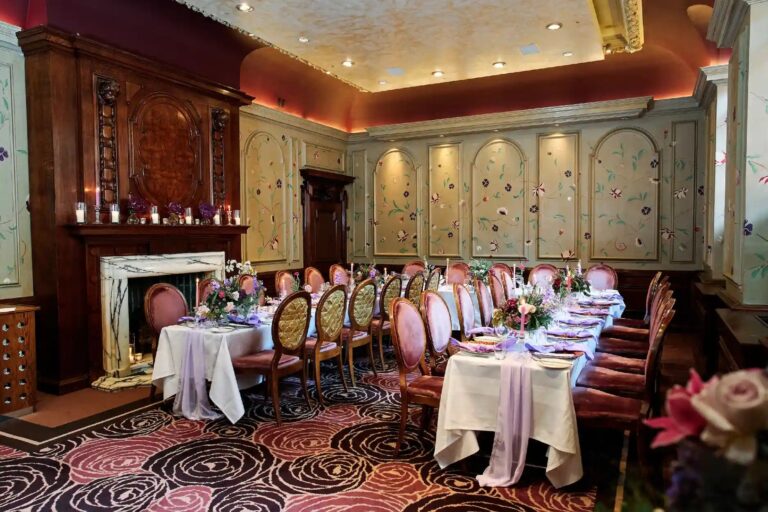 The Eden Room set with a long dressed table, its hand-painted floral wall panels and carved fireplace behind, The Roseate Reading