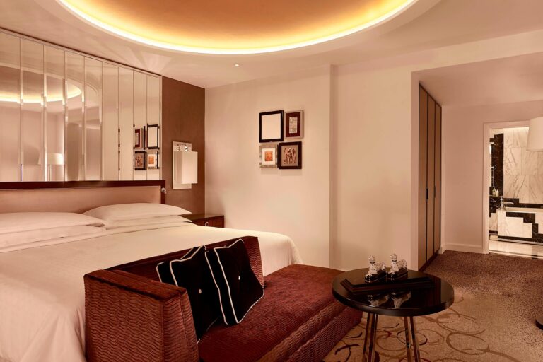 A bedroom with a mirrored headboard wall, a glowing ceiling cove and a burgundy day bed, The Sheraton Park Lane Hotel