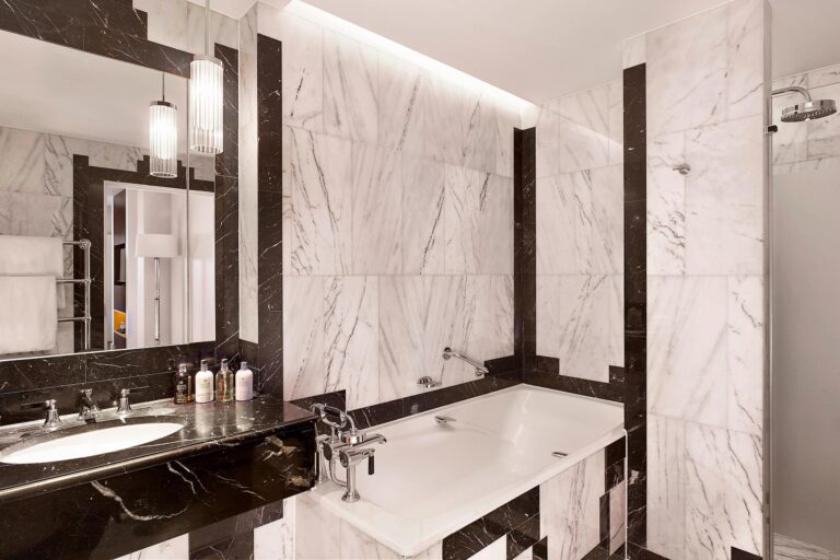 A marble bathroom with a bath, black-edged panelling and glass pendant lights, The Sheraton Park Lane Hotel