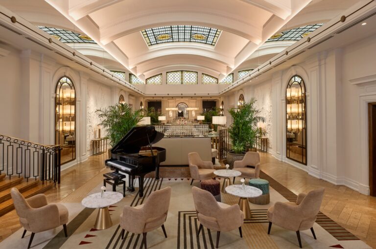 The Palm Court lounge under its barrel-vaulted ceiling and skylights, with a grand piano and low armchairs, The Sheraton Park Lane Hotel