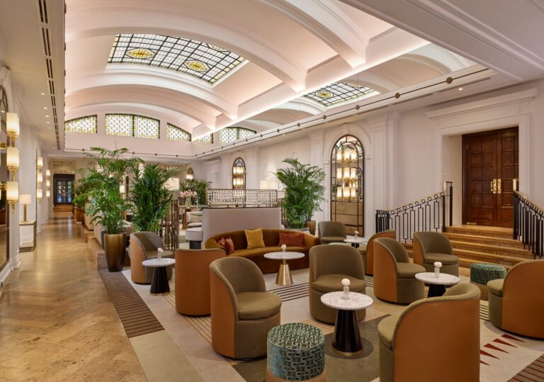 Curved banquettes and palms in the Palm Court, with the staircase and arched windows behind, The Sheraton Park Lane Hotel