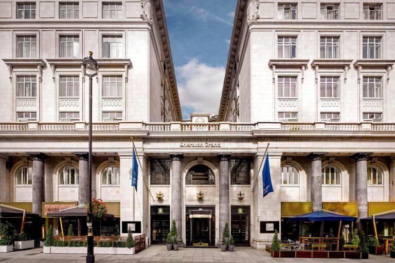 The hotel front on Piccadilly, with its pale stone facade, flags over the entrance and terrace seating at street level, The Sheraton Park Lane Hotel