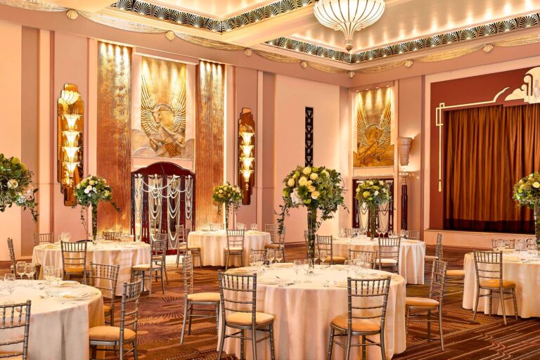 The Ballroom set for a wedding reception, with round tables, chiavari chairs, tall floral centrepieces and gilded Art Deco wall panels, The Sheraton Park Lane Hotel