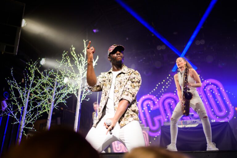 A singer and saxophonist performing as the COCO line-up under blue stage lighting, The Sway Allstars