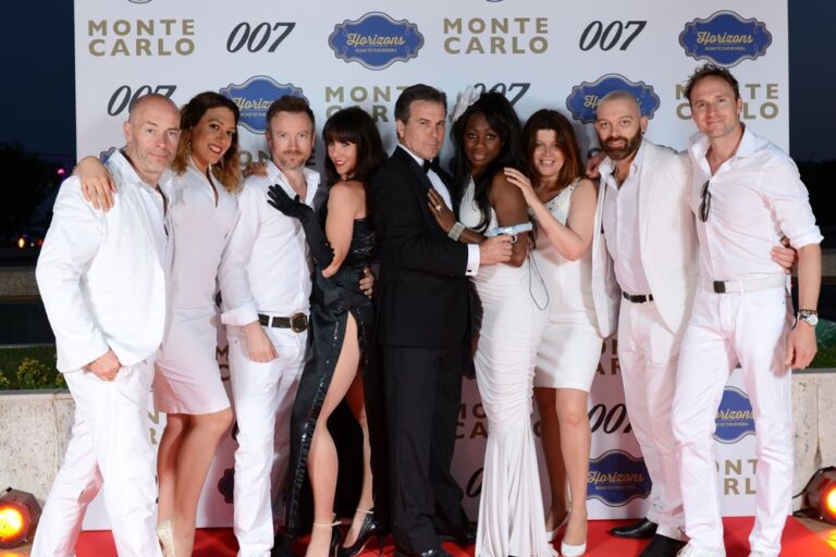 The band in white outfits in front of a 007 Monte Carlo backdrop, The Sway Allstars