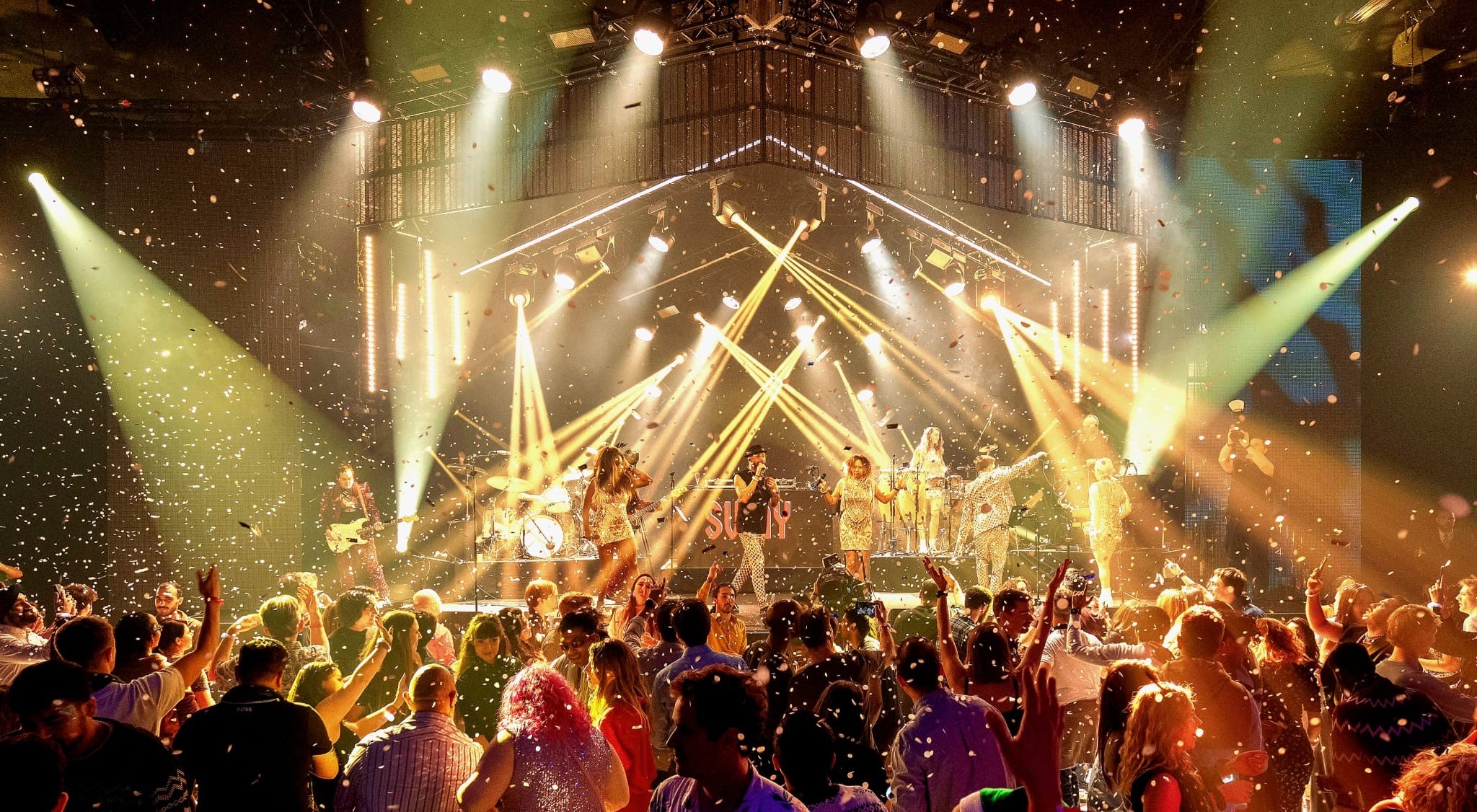 The band on stage with stage lighting and confetti over a dancing crowd, The Sway Allstars