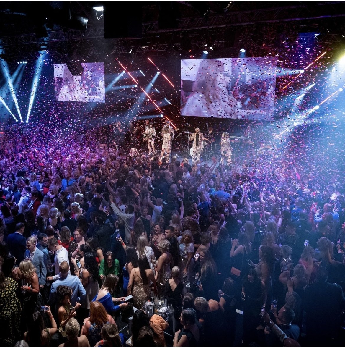 A packed dance floor in front of the band on a large stage with video screens, The Sway Allstars