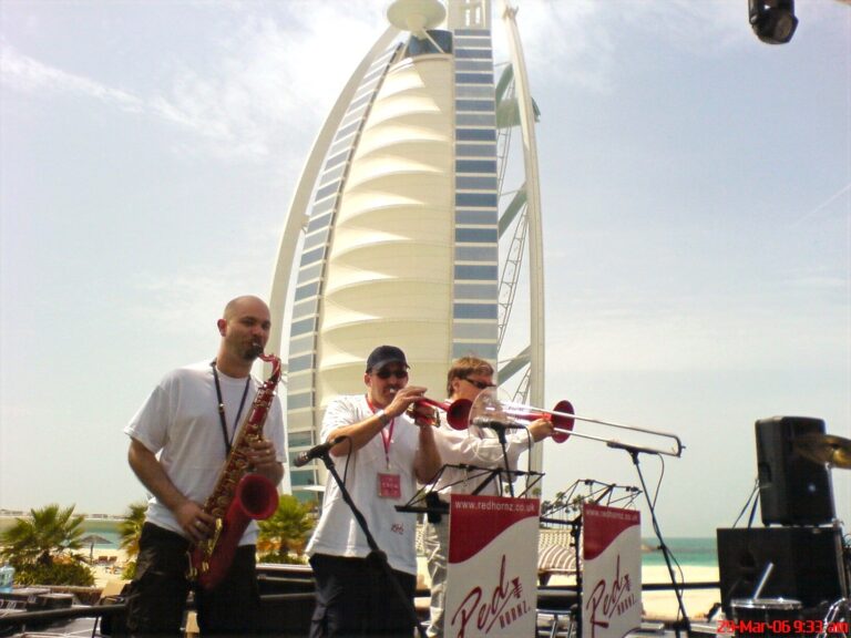 Sax, trumpet and percussion playing outdoors with the Burj Al Arab behind, The Sway Allstars