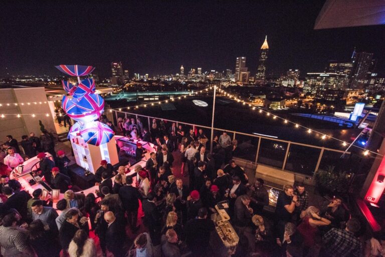 A rooftop party at night with a crowd below a lit sculpture, The Sway Allstars