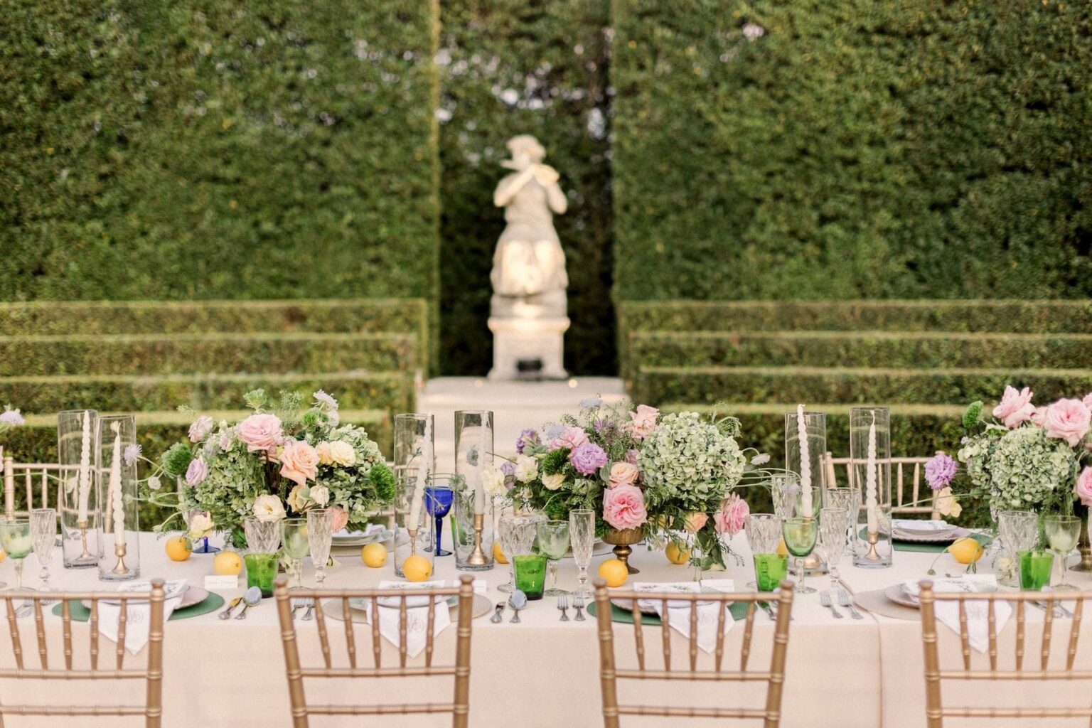 A long dinner table set in the Formal Garden before the hedges and statues