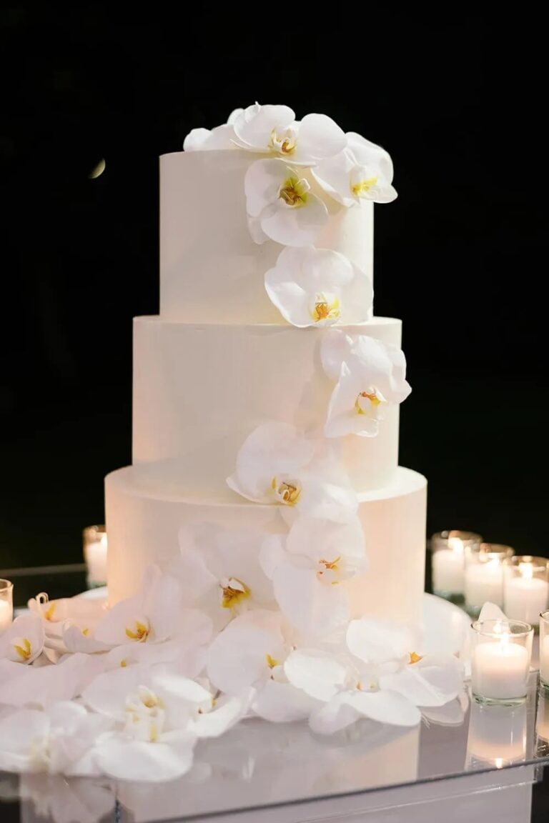 A white wedding cake with white flowers at night, The Wedding Atelier