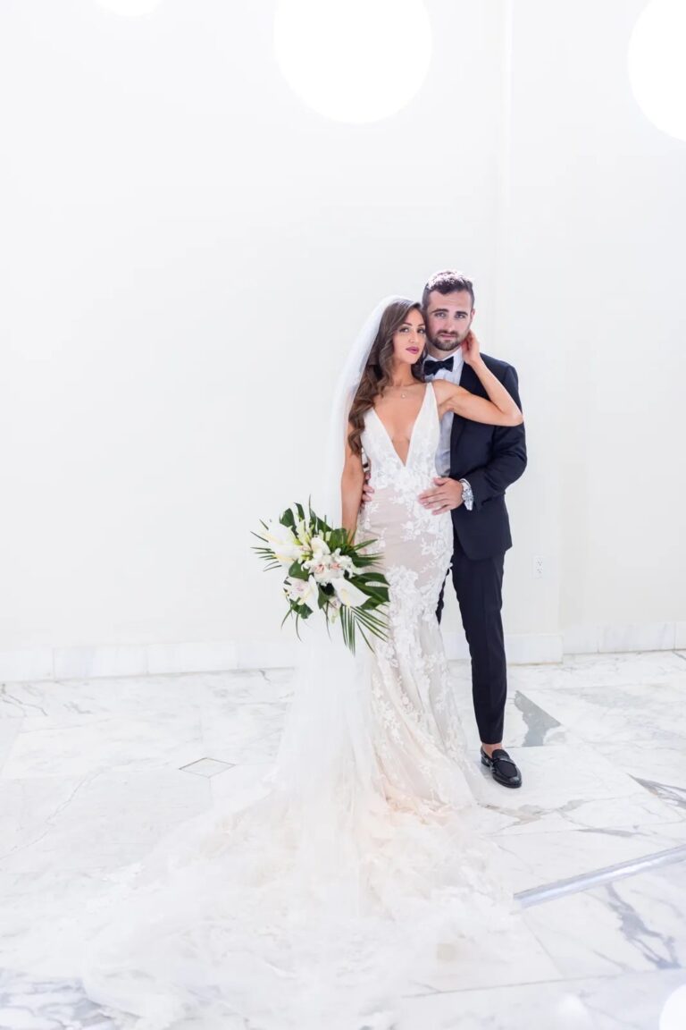 A bride and groom in white against a pale backdrop, The Wedding Atelier