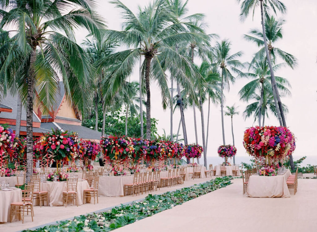A pink and orange flower aisle leading to Thai-style pavilions among palms