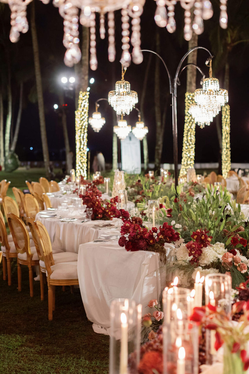 Hanging crystal chandeliers over the reception tables among red and white flowers, The Wedding Bliss - Thailand