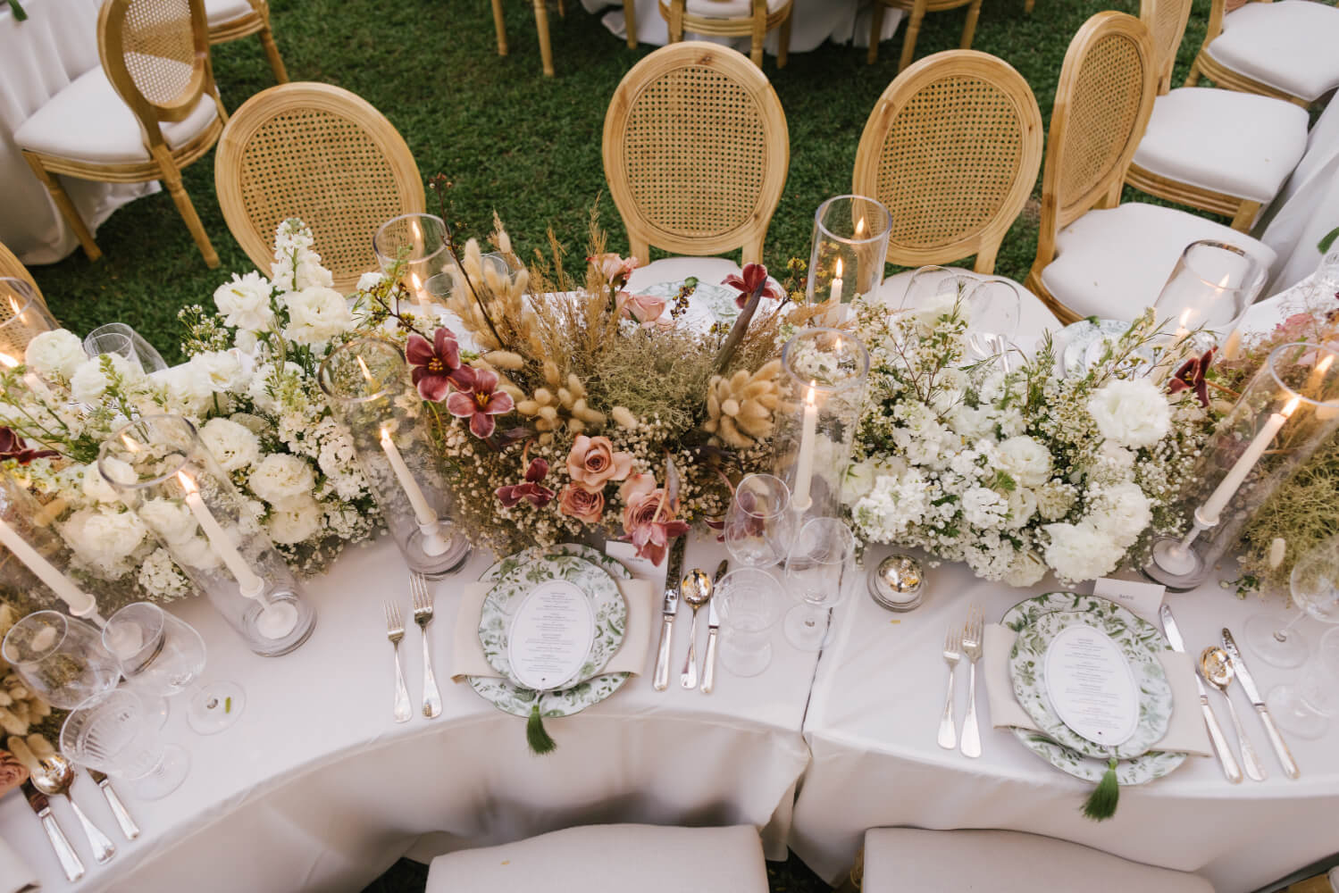 A curved dining table dressed in white and blush flowers with candles and gold chairs, The Wedding Bliss - Thailand