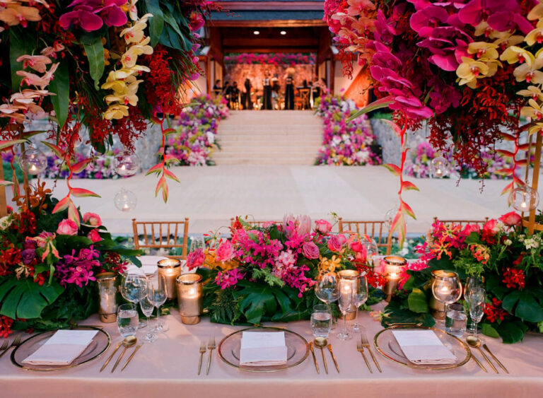 A banquet table edged with bright tropical flowers beneath a draped stage, The Wedding Bliss - Thailand