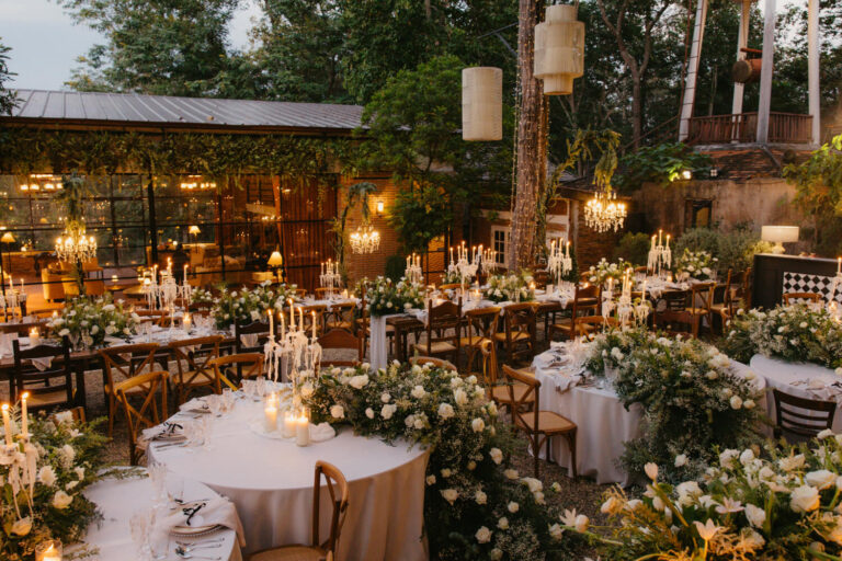 A timber pavilion lit for dinner, with round tables and flowers in the garden, The Wedding Bliss - Thailand