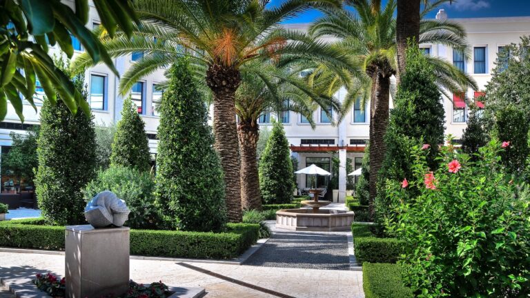 The garden courtyard with palms, a sculpture and the stone fountain, box hedging in the foreground, The Westin Valencia