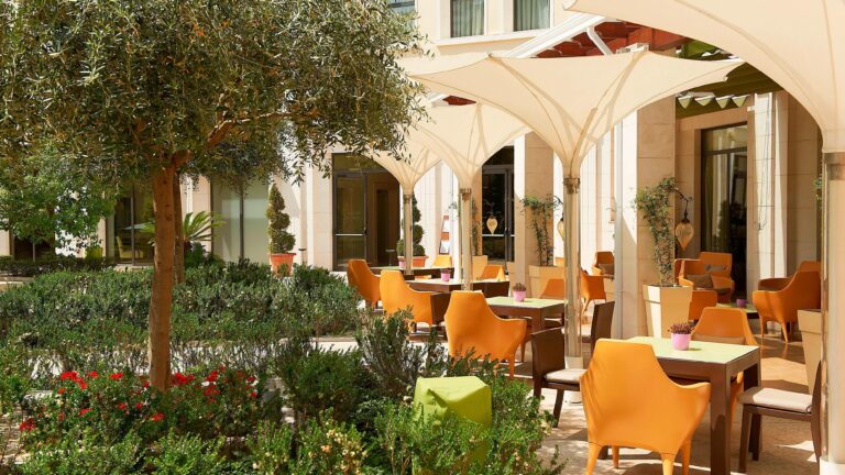 A garden terrace with olive trees, orange chairs and parasols among the planting, The Westin Valencia