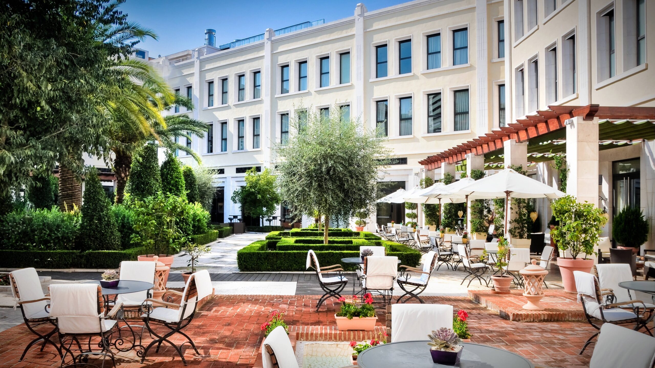 The garden courtyard laid with cafe tables and parasols beneath a pergola, the Modernista facade behind, The Westin Valencia