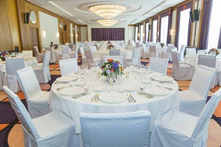 A wedding banquet set in the ballroom, white chair covers and floral centrepieces under the chandeliers, The Westin Valencia