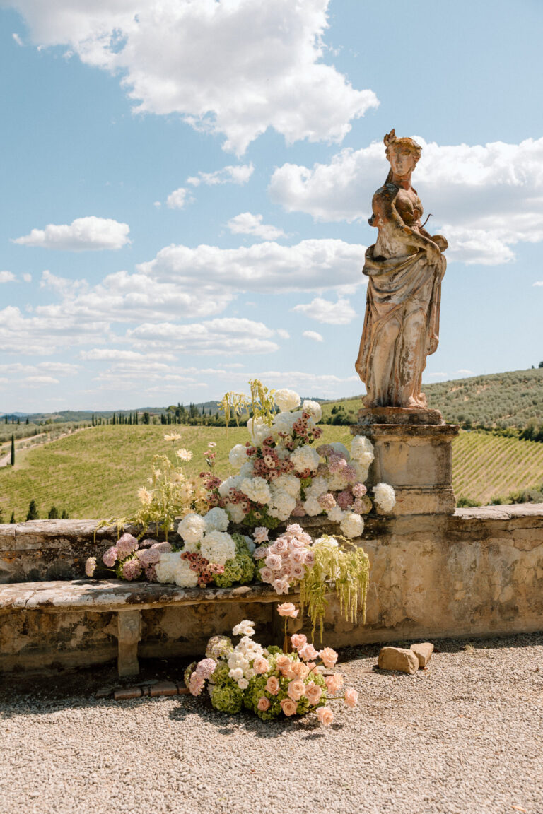 Flowers banked at the foot of a statue above the Tuscan hills, Villa Corsini a Mezzomonte, TheKnotInItaly
