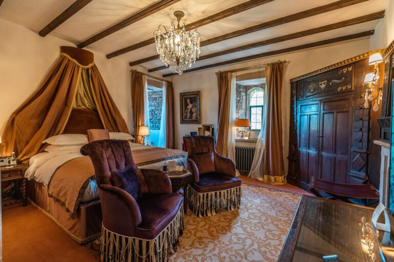 A beamed Deluxe bedchamber with canopied bed and velvet armchairs, Thornbury Castle