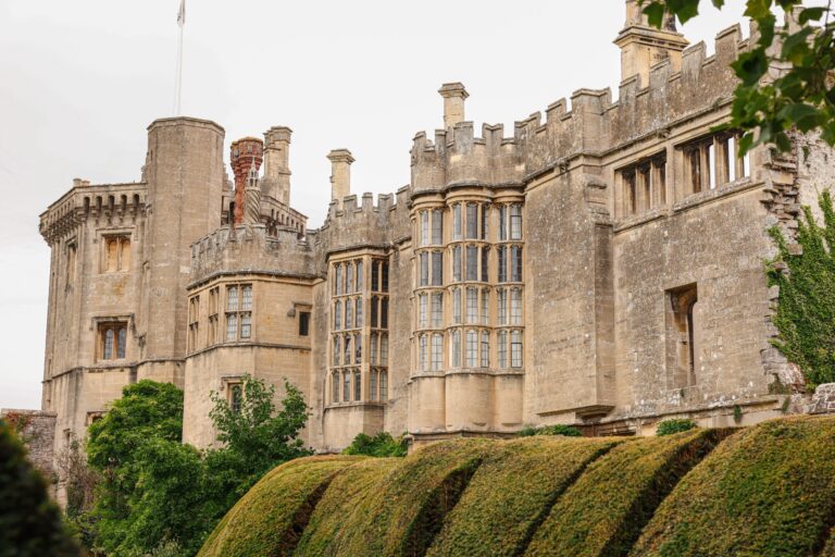 Battlemented towers and oriel windows rising behind clipped yew topiary, Thornbury Castle