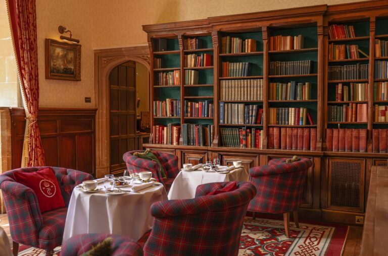 The library, with bookcases and tartan armchairs around laid tables, Thornbury Castle