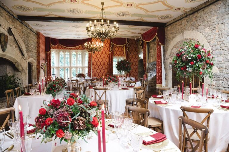 Round tables with red flowers and candles laid for a wedding breakfast in the Tudor Hall, Thornbury Castle