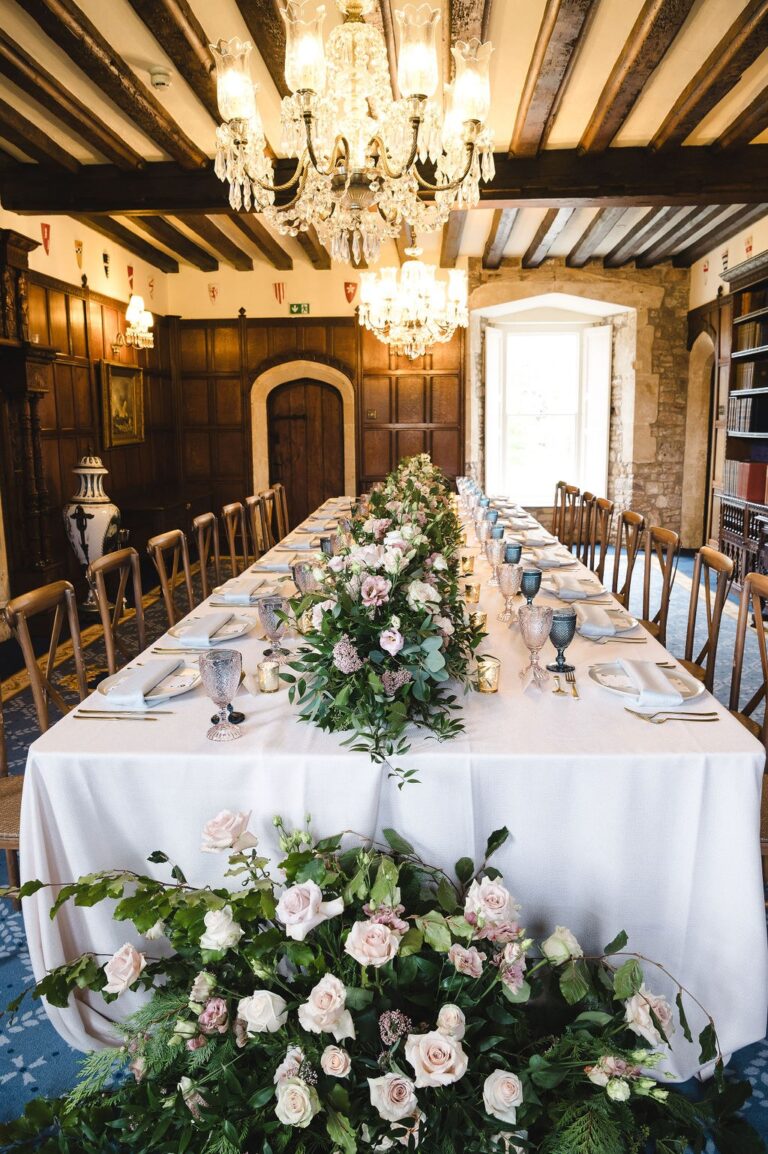 A long table with white flowers set beneath beams and a chandelier in a panelled room, Thornbury Castle