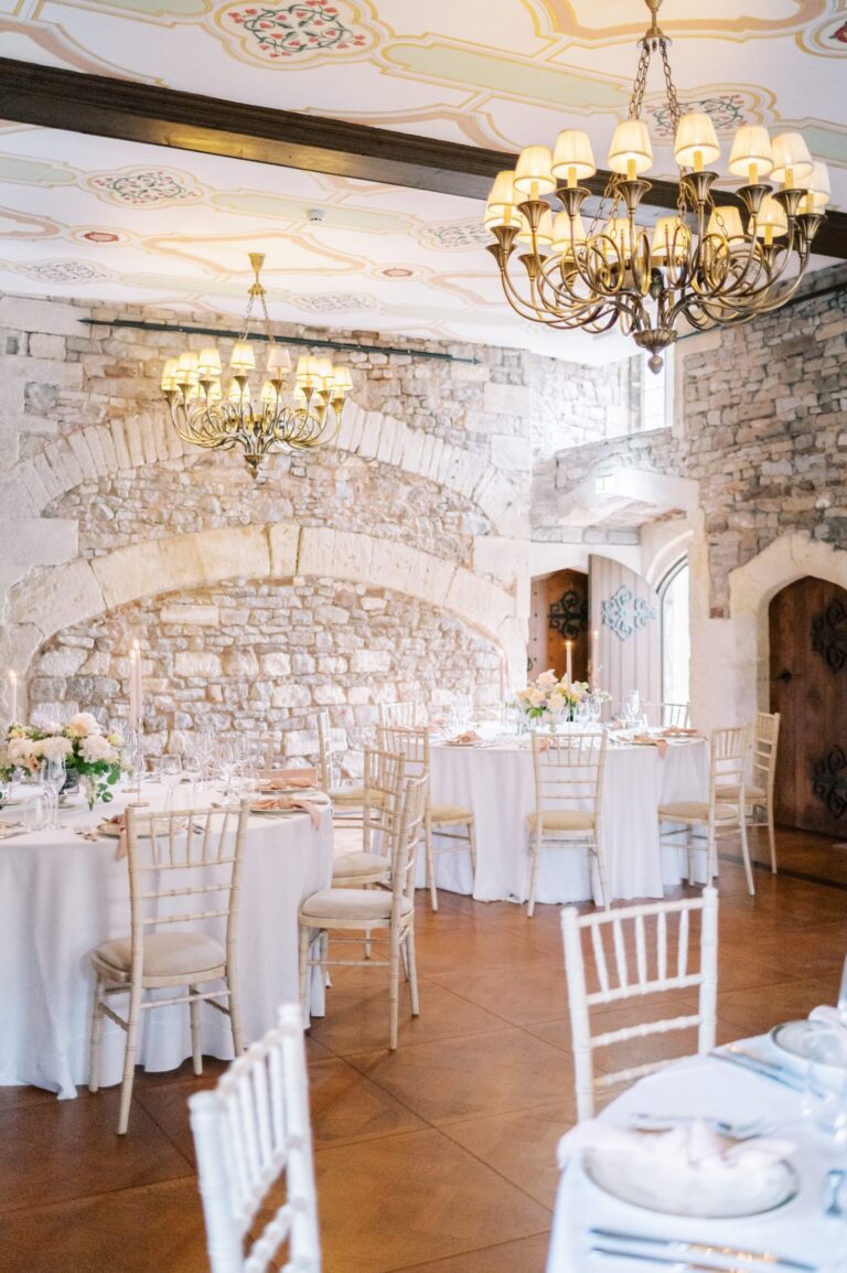 Tables laid for a reception in a whitewashed room with chandeliers, Thornbury Castle