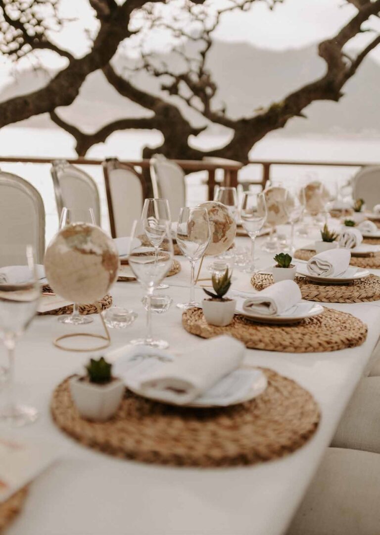 A reception table laid under the ancient milkwood canopy, rattan chargers and glassware, Tintswalo Atlantic