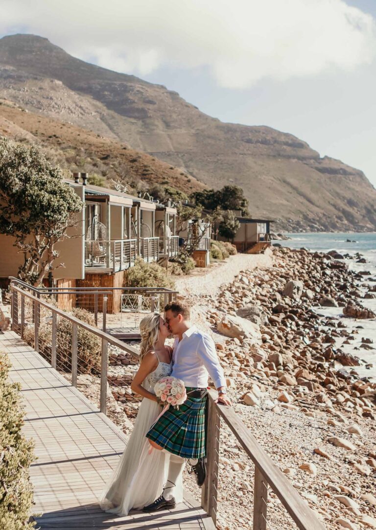 The couple on the raised boardwalk, island suites and the coastline running away behind, Tintswalo Atlantic