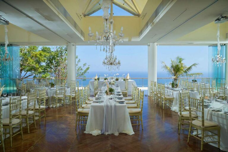 Long tables laid in the Heaven Room with the ocean beyond the glass, Tirtha Bridal