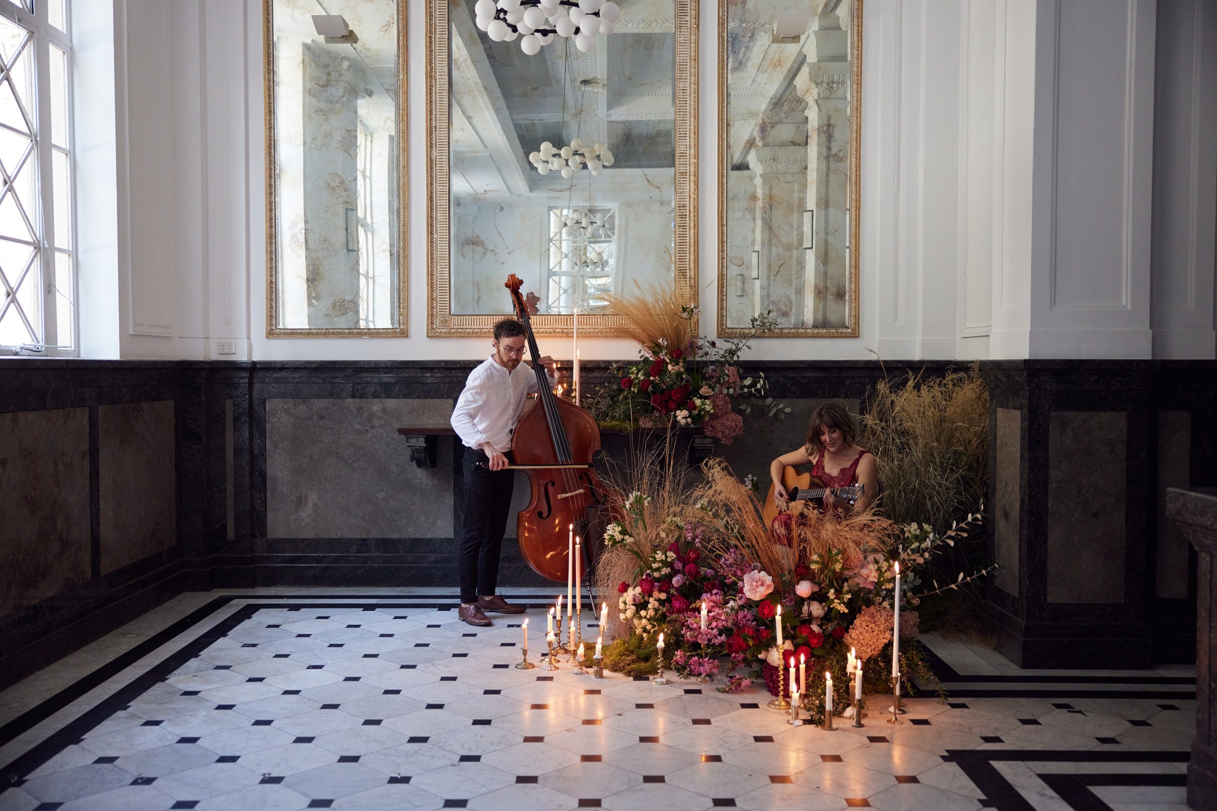 Double bass and guitar among floral installations in a grand hall, Tobi Tobi