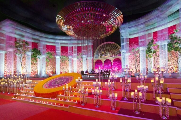 A pink and orange ceremony mandap beneath a crystal chandelier, Tomas De Bruyne