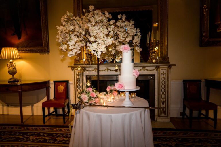 A tiered wedding cake with pink roses and the ceremonial sword in front of a marble fireplace, Trinity House on Tower Hill