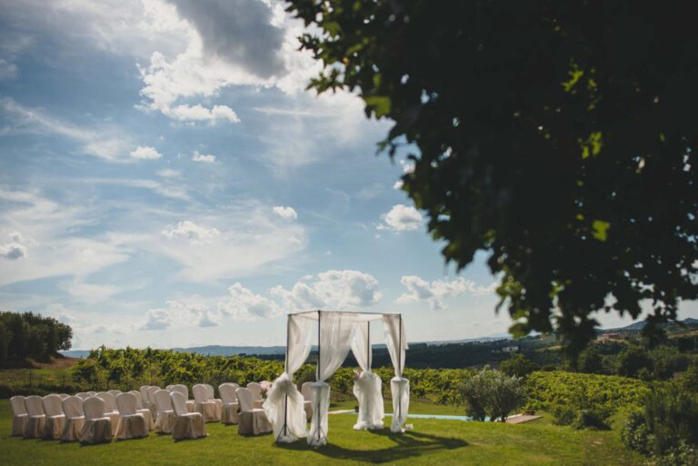 A white draped canopy and rows of white chairs set on a lawn above the Tuscan countryside, Tuscan DMC
