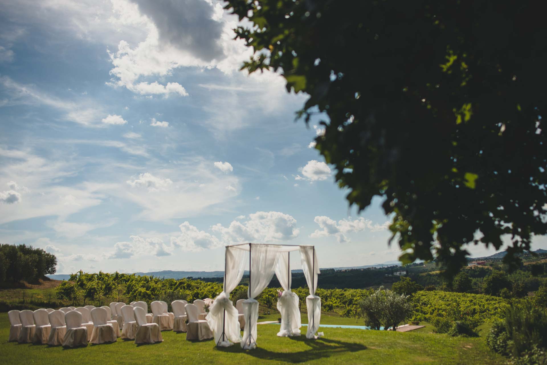 A white draped canopy and rows of white chairs set on a lawn above the Tuscan countryside, Tuscan DMC