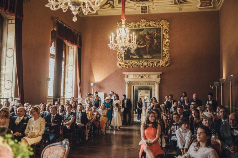 Guests seated for a ceremony in a frescoed hall with chandeliers and an oil painting, Tuscan DMC