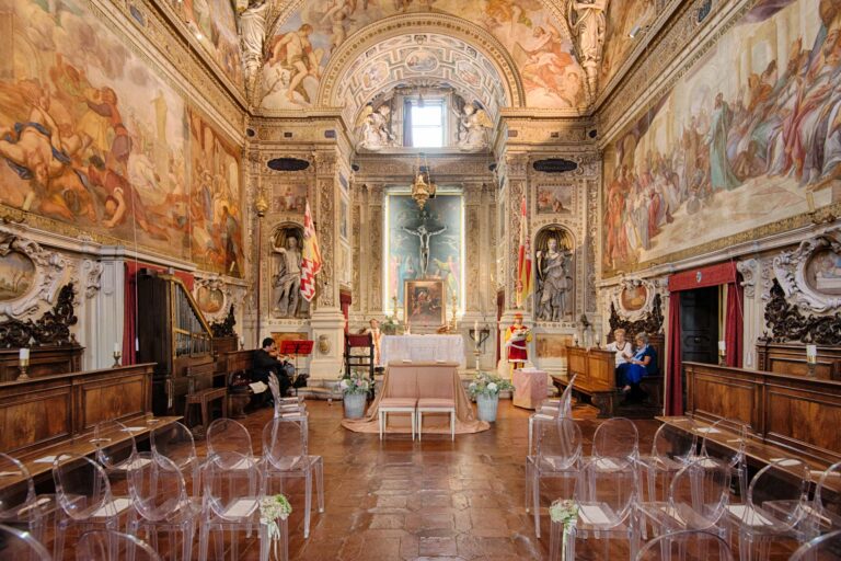 A frescoed chapel set for a ceremony with clear chairs and pale flowers, Tuscan DMC